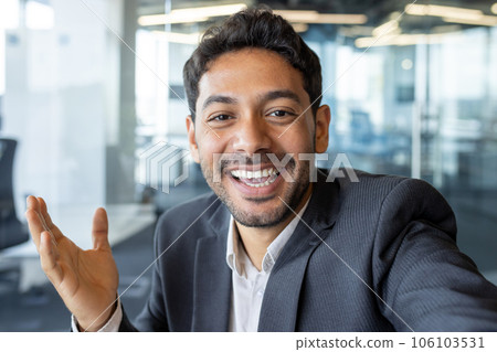 Video call friendly conversation, arab businessman inside office talking with friends and colleagues at workplace, man using app on phone, smiling and friendly waving at camera. 106103531