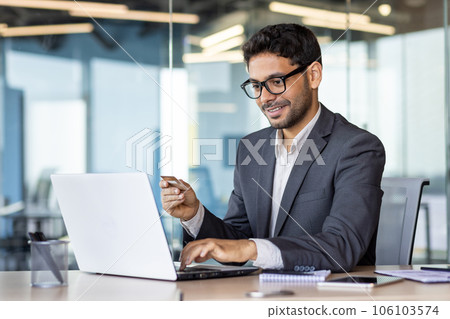 Happy successful businessman with bank credit card inside office at workplace, man using laptop for online shopping and money transfer. Happy successful businessman with bank credit card inside office at workplace, man using laptop for online shopping and money transfer. 106103574