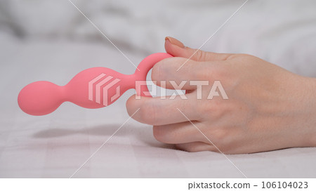 Close-up of a female hand with pink anal beads lying in bed. Close-up of a female hand with pink anal beads lying in bed. 106104023