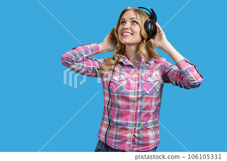 Portrait of young blond woman listening to music in headphones. Isolated on vivid blue background. Portrait of young blond woman listening to music in headphones. Isolated on vivid blue background. 106105331