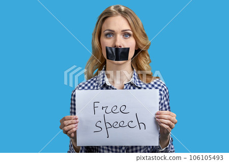 Young blonde woman protester with taped mouth holding banner with inscription free speech. Silenced woman on blue background. 106105493
