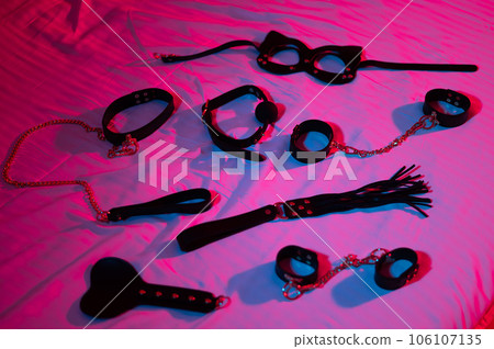 BDSM set on white sheet in blue red neon light. BDSM set on white sheet in blue red neon light. 106107135