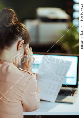 Seen from behind modern woman with documents having headache 106107633
