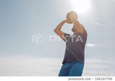 A middle-aged man aims to throw a basketball into the basket. A guy doing sports against the background of a blue sky in the rays of the setting sun 106107700