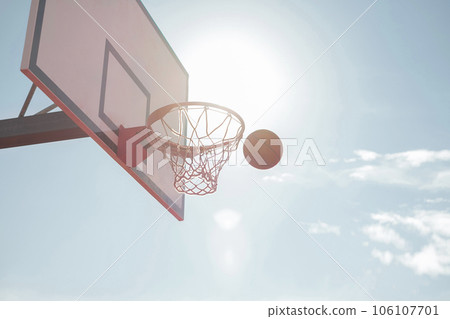 The ball flies into the basketball hoop against the background of the sky and the setting sun. Big White Basketball Shield The ball flies into the basketball hoop against the background of the sky and the setting sun. Big White Basketball Shield 106107701