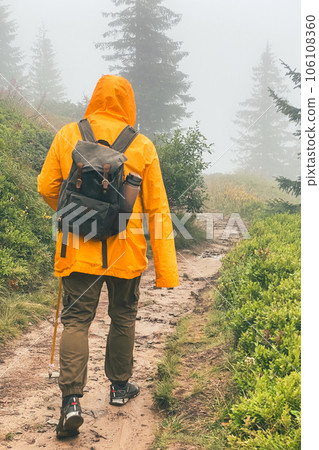 man in yellow raincoat at foggy mountain trail 106108360
