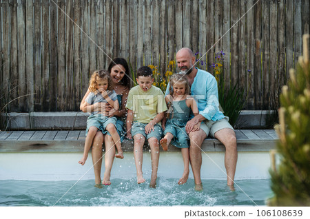 Cheerful family with three kids having fun together sitting by a pool. 106108639