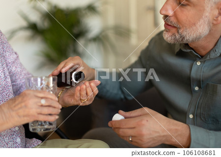 Adult son giving pills to his ill mother, helping to take medication safely, at the right time. Adult son giving pills to his ill mother, helping to take medication safely, at the right time. 106108681