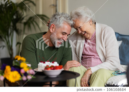 Mature man celebrating with his senior mother at her apartment. 106108684