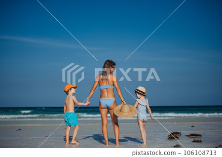 Rear view of a mother with little girl and boy walking on the beach. 106108713