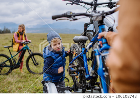 Littlle boy helping father attache a bicycle on bike carrier. 106108748