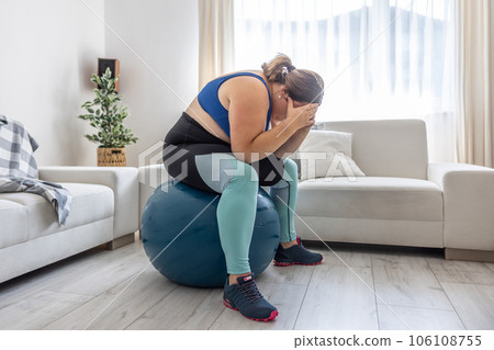 Frustrated obese woman sitting on a swiss ball and crying because of her overweight 106108755