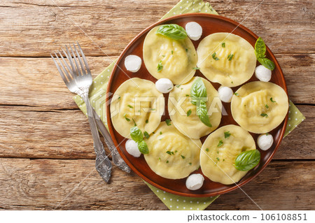 Cappellacci fresh filled pasta made with a delicious filling mozzarella and basil closeup on the plate on the wooden. Horizontal top view Cappellacci fresh filled pasta made with a delicious filling mozzarella and basil closeup on the plate on the wooden. Horizontal top view 106108851