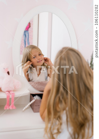 Happy child girl of seven years old puts on earrings in front of the mirror Happy child girl of seven years old puts on earrings in front of the mirror 106110282