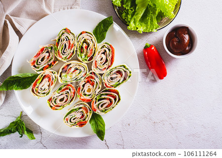 Italian rolled sandwiches with lettuce, ham and baked peppers in pita bread on a plate top view Italian rolled sandwiches with lettuce, ham and baked peppers in pita bread on a plate top view 106111264