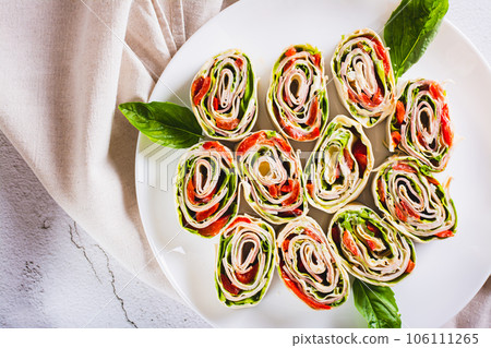Close up of rolled sandwiches with lettuce, ham and baked peppers in pita bread on a plate top view Close up of rolled sandwiches with lettuce, ham and baked peppers in pita bread on a plate top view 106111265