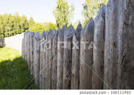 Close-up of a wooden wall made of sharp wooden stakes on a sunny summer day. Clear blue sky with occasional clouds. Soft focus. Protection, security, state border. Close-up of a wooden wall made of sharp wooden stakes on a sunny summer day. Clear blue sky with occasional clouds. Soft focus. Protection, security, state border. 106111493