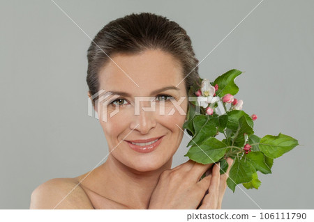 Smiling mid adult woman holding spring flowers. Cosmetology, facial treatment and skincare concept 106111790