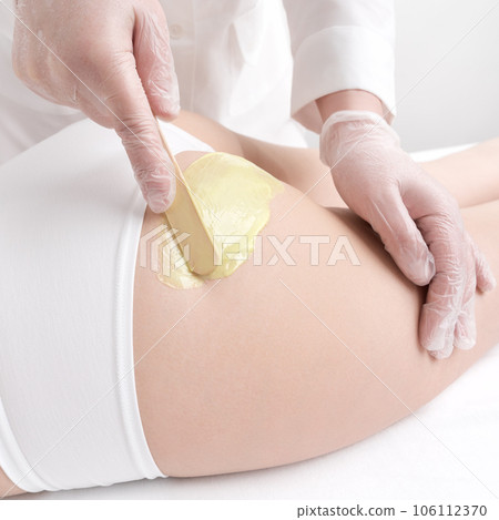 Closeup hand applying hot wax on woman buttocks using spatula during hair removal procedure. Waxing process, depilation with green hot wax in professional beauty salon. Part of photo series Closeup hand applying hot wax on woman buttocks using spatula during hair removal procedure. Waxing process, depilation with green hot wax in professional beauty salon. Part of photo series 106112370