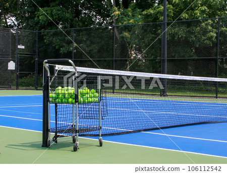 Blue tennis court with a cart of tennis balls 106112542