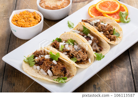 Pork carnitas tacos with onion and cilantro served with rice and refried beans Pork carnitas tacos with onion and cilantro served with rice and refried beans 106113587