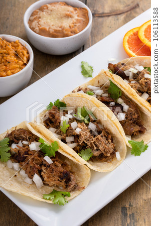 Pork carnitas tacos with onion and cilantro served with rice and refried beans 106113588