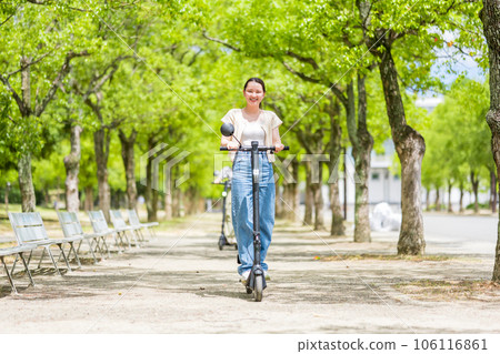 A young and cute woman refreshingly running on an electric kickboard on a beautiful green tree-lined street | Electric kickboard image A young and cute woman refreshingly running on an electric kickboard on a beautiful green tree-lined street | Electric kickboard image 106116861