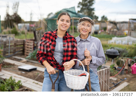 Two smiling casual women neighbors of different ages making arrangements during the vegetable garden sowing season on sunny day of spring Two smiling casual women neighbors of different ages making arrangements during the vegetable garden sowing season on sunny day of spring 106117157