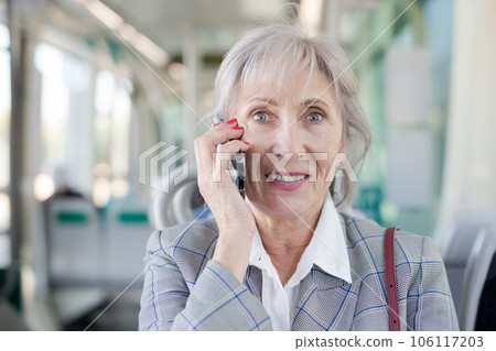 Senior woman having telephone conversation in tram 106117203