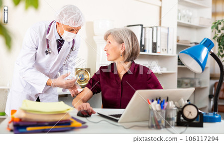 Man doctor vaccinating senior woman in office 106117294