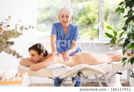 Elderly woman doing back massage to young woman Elderly woman doing back massage to young woman 106117451