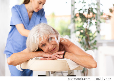 Smiling senior woman lying on couch during back massage Smiling senior woman lying on couch during back massage 106117486
