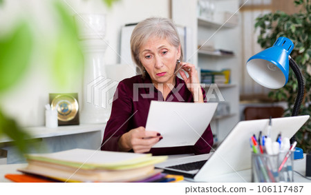 Frustrated aged female entrepreneur sitting at office desk with papers Frustrated aged female entrepreneur sitting at office desk with papers 106117487