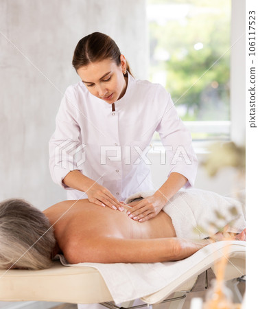 Skilled young masseuse doing back pain relief massage to elderly woman Skilled young masseuse doing back pain relief massage to elderly woman 106117523