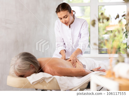 Skilled young masseuse doing back pain relief massage to elderly woman Skilled young masseuse doing back pain relief massage to elderly woman 106117555