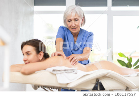 Experienced older professional masseuse doing back massage to young woman Experienced older professional masseuse doing back massage to young woman 106117557