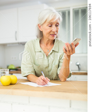 Positive senior woman talking on phone and making notes 106117694