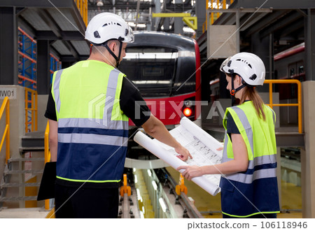 Young caucasian engineer man and woman or worker looking blueprint and checking electric train. Young caucasian engineer man and woman or worker looking blueprint and checking electric train. 106118946