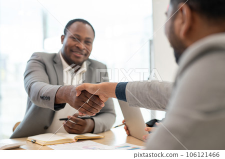 A satisfied African American CEO shaking hands with an Asian male business partner after a meeting 106121466