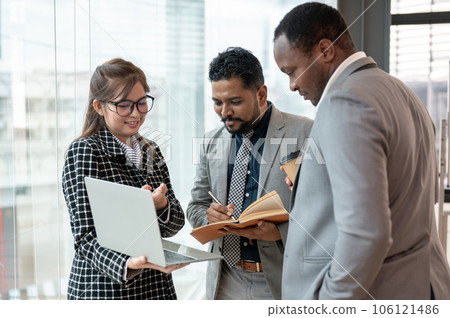 A multiracial group of business people. discussing work while standing in a company corridor A multiracial group of business people. discussing work while standing in a company corridor 106121486