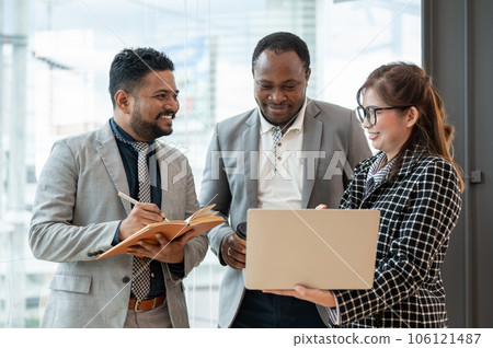 A multiracial group of business people is discussing work while standing in a company corridor 106121487