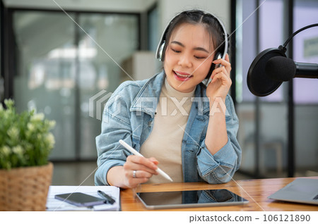 A happy Asian female radio host is interviewing a guest over the phone while broadcasting A happy Asian female radio host is interviewing a guest over the phone while broadcasting 106121890