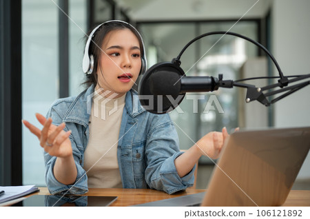 A professional Asian female radio host or podcaster is speaking into a microphone 106121892