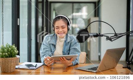 A cheerful Asian female radio host speaking into a microphone, and recording her podcast A cheerful Asian female radio host speaking into a microphone, and recording her podcast 106121896