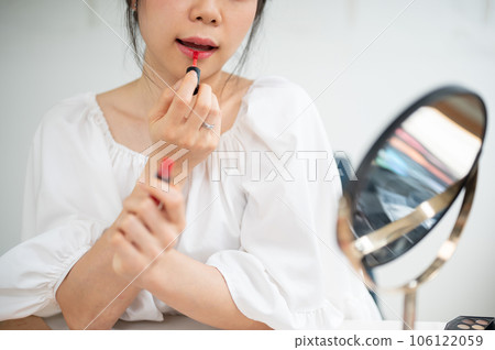 Close-up image of a pretty Asian female applies lipstick on her lips, doing her daily makeup. 106122059