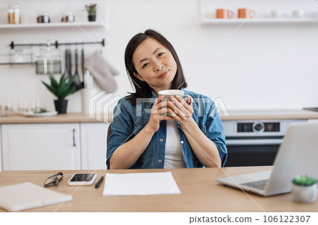 Adult posing with drink while working on laptop in kitchen 106122307