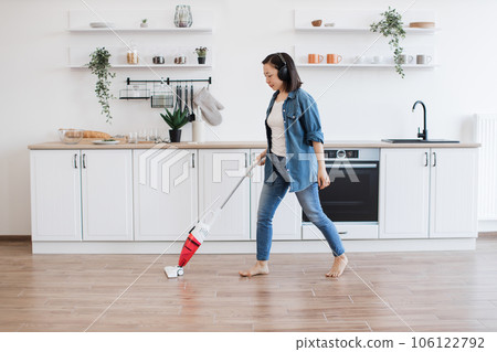 Asian lady using upright vacuum with music in headphones Asian lady using upright vacuum with music in headphones 106122792
