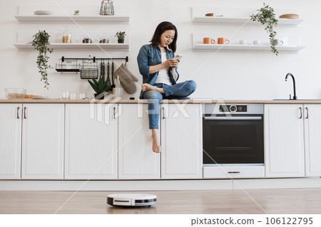 Lady scrolling on mobile while robot dust collector cleaning Lady scrolling on mobile while robot dust collector cleaning 106122795