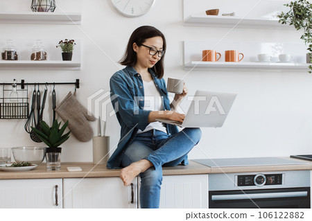 Lady with tea cup teleworking from home using laptop 106122882
