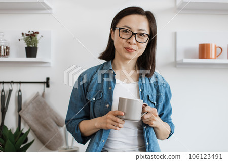 Asian lady in glasses smiling with mug of tea in hand 106123491